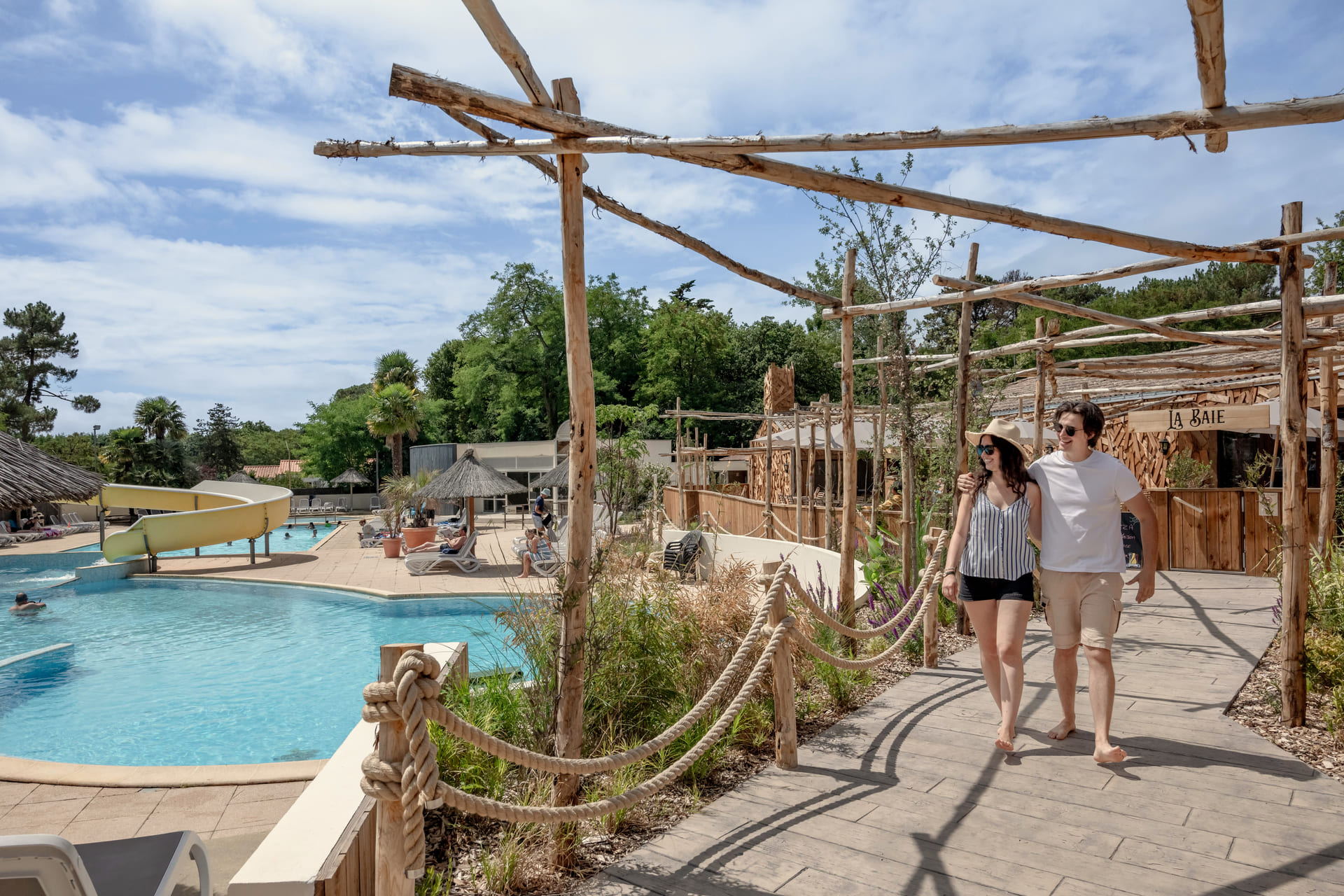 La Baie water park at Camping Au Bois des Biches, featuring large outdoor pools, slides, and a sunny relaxation area.