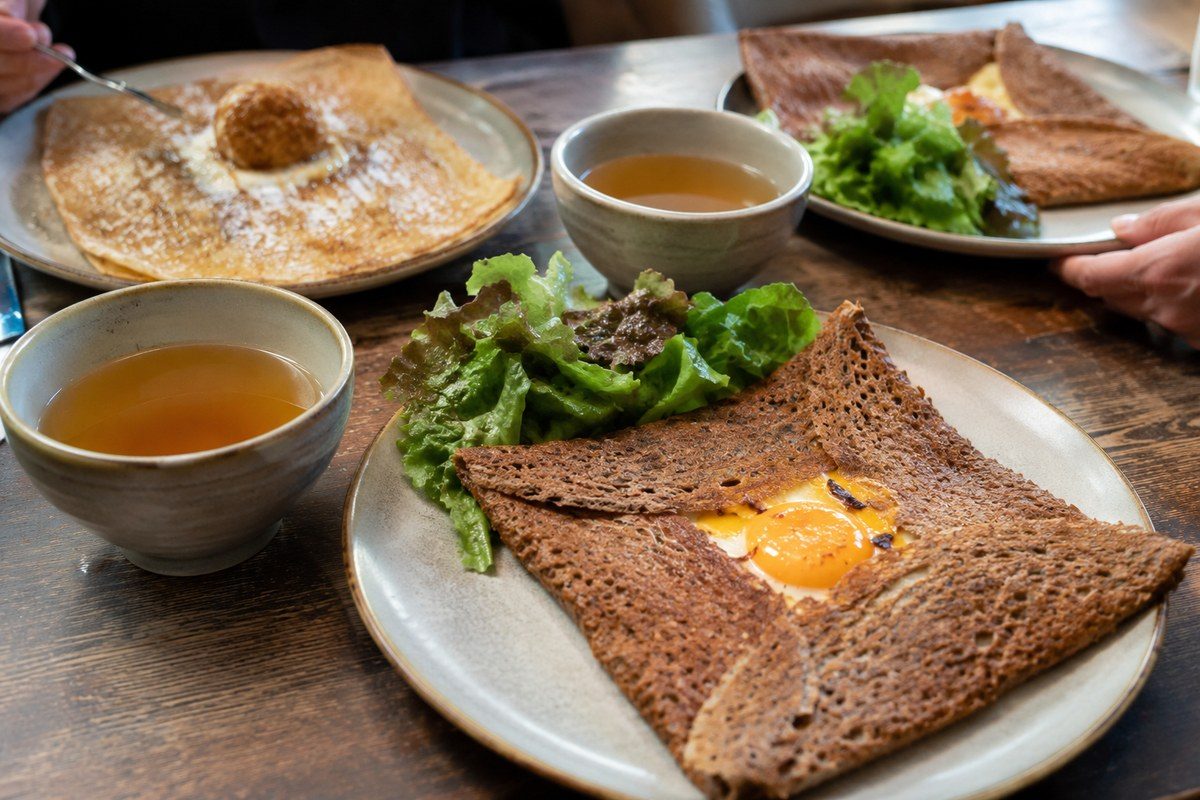 Galettes de sarrasin et bolées de cidre partagées autour d'une table dans une crêperie