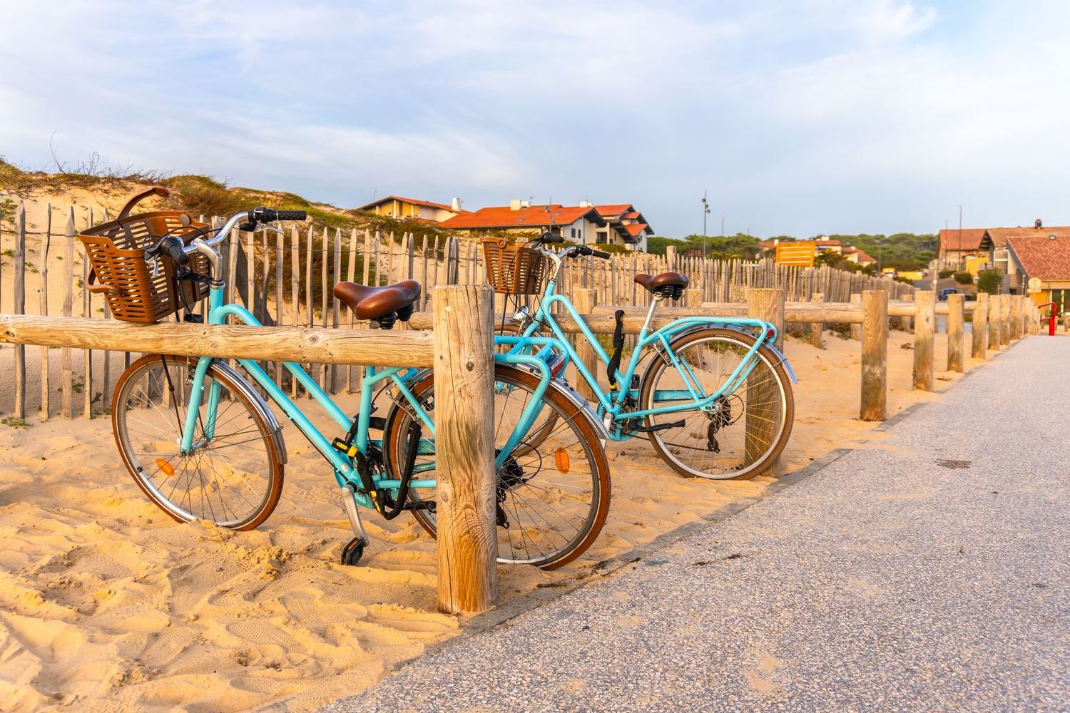 Deux vélos bleus à paniers garés contre une clôture de dune, au bord d'une piste